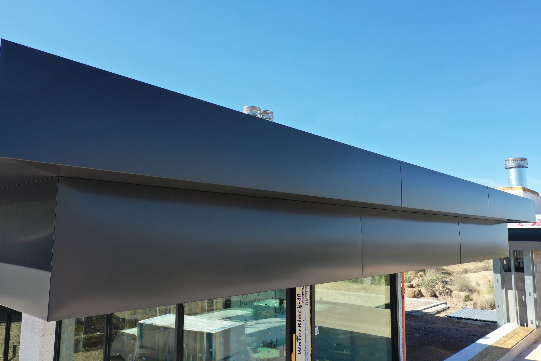 Custom charcoal metal fascia wrapping the roofline of a modern desert build