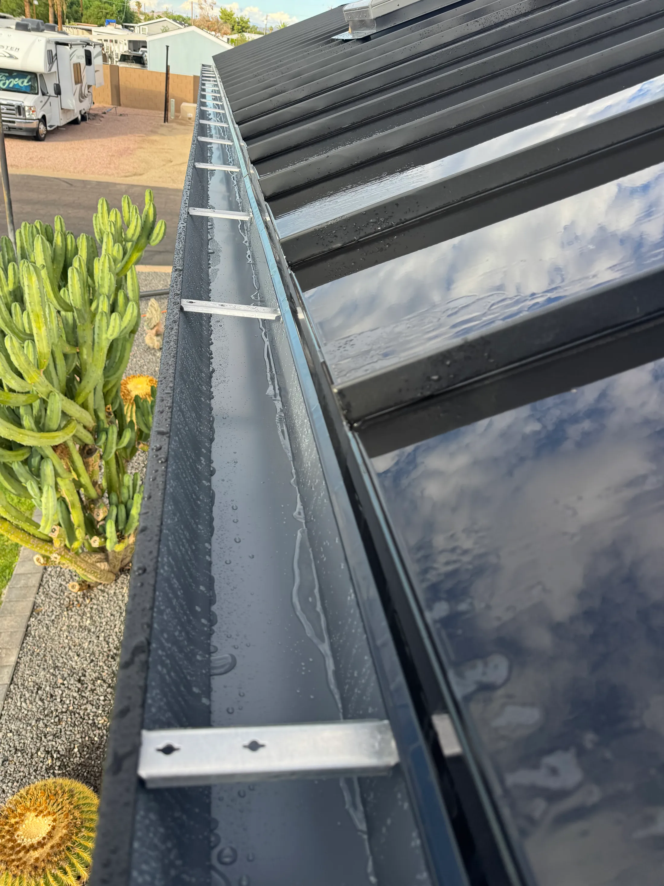 Black seamless gutter with hidden hangers along a metal roof edge